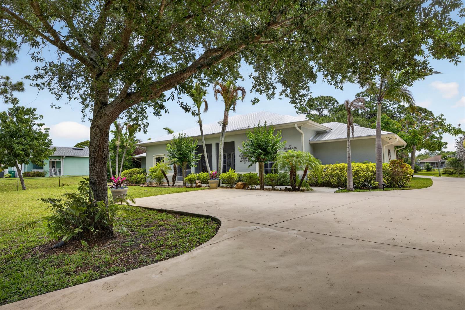 A light-colored house with a metal roof sits behind a large concrete driveway — 5606 Silver Oak Drive, Fort Pierce FL 34982, FORT PIERCE, FL