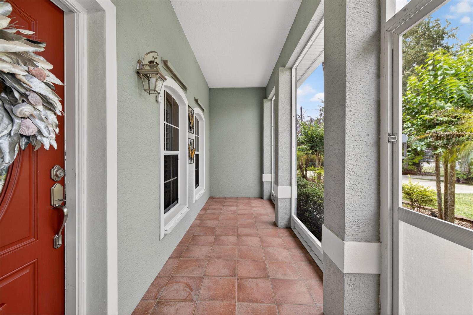 A covered porch features a red front door, tiled flooring, and screened-in walls — 5606 Silver Oak Drive, Fort Pierce FL 34982, FORT PIERCE, FL