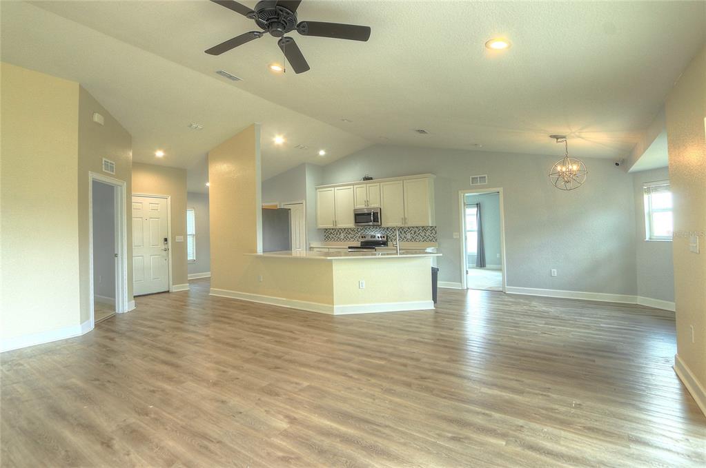 An open-concept living area features a kitchen with white cabinets, a breakfast bar, and wood-look flooring — 110 PLUM AVENUE, FROSTPROOF, FL
