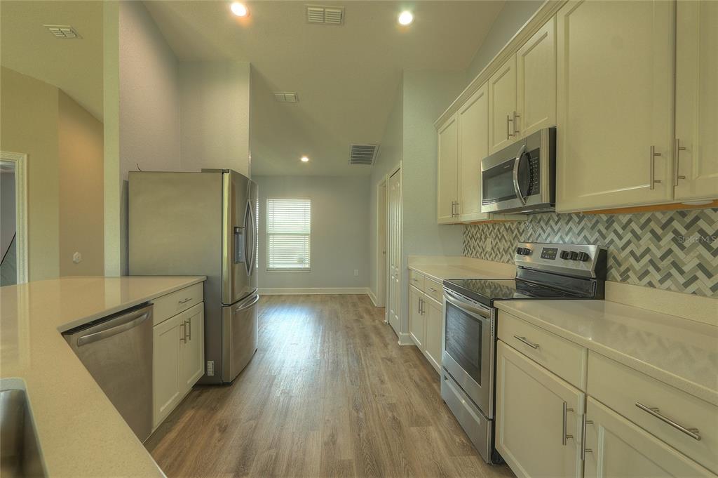 A kitchen with white cabinets, stainless steel appliances, and a patterned tile backsplash — 110 PLUM AVENUE, FROSTPROOF, FL