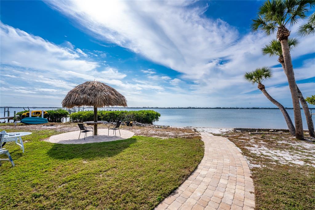 A grassy waterfront yard features a tiki hut, a stone walkway, and two palm trees — 470 S MCCALL ROAD UNIT 10, ENGLEWOOD, FL