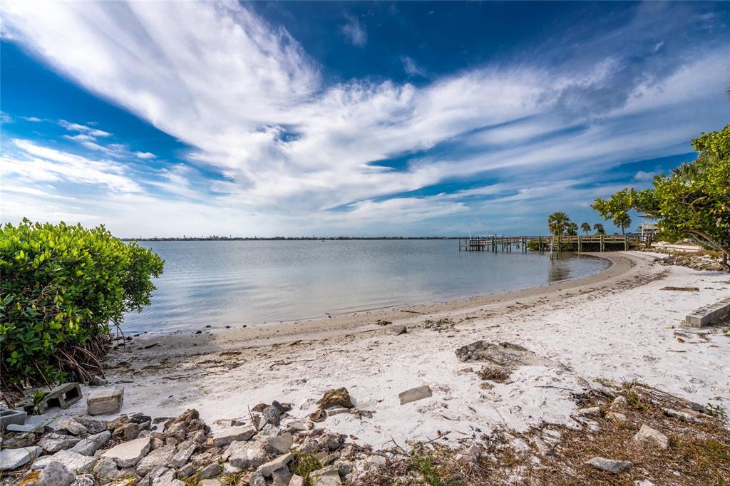 A sandy beach borders a calm bay with a wooden dock under a cloudy sky — 470 S MCCALL ROAD UNIT 10, ENGLEWOOD, FL