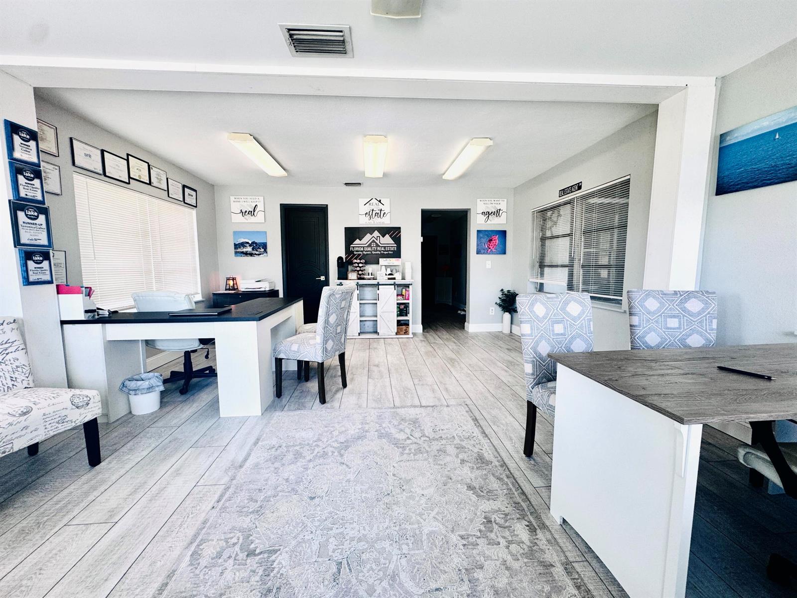 A bright real estate office features desks, patterned chairs, light wood-look flooring, and wall decor — 206 SW 3rd Street, Okeechobee FL 34974, OKEECHOBEE, FL