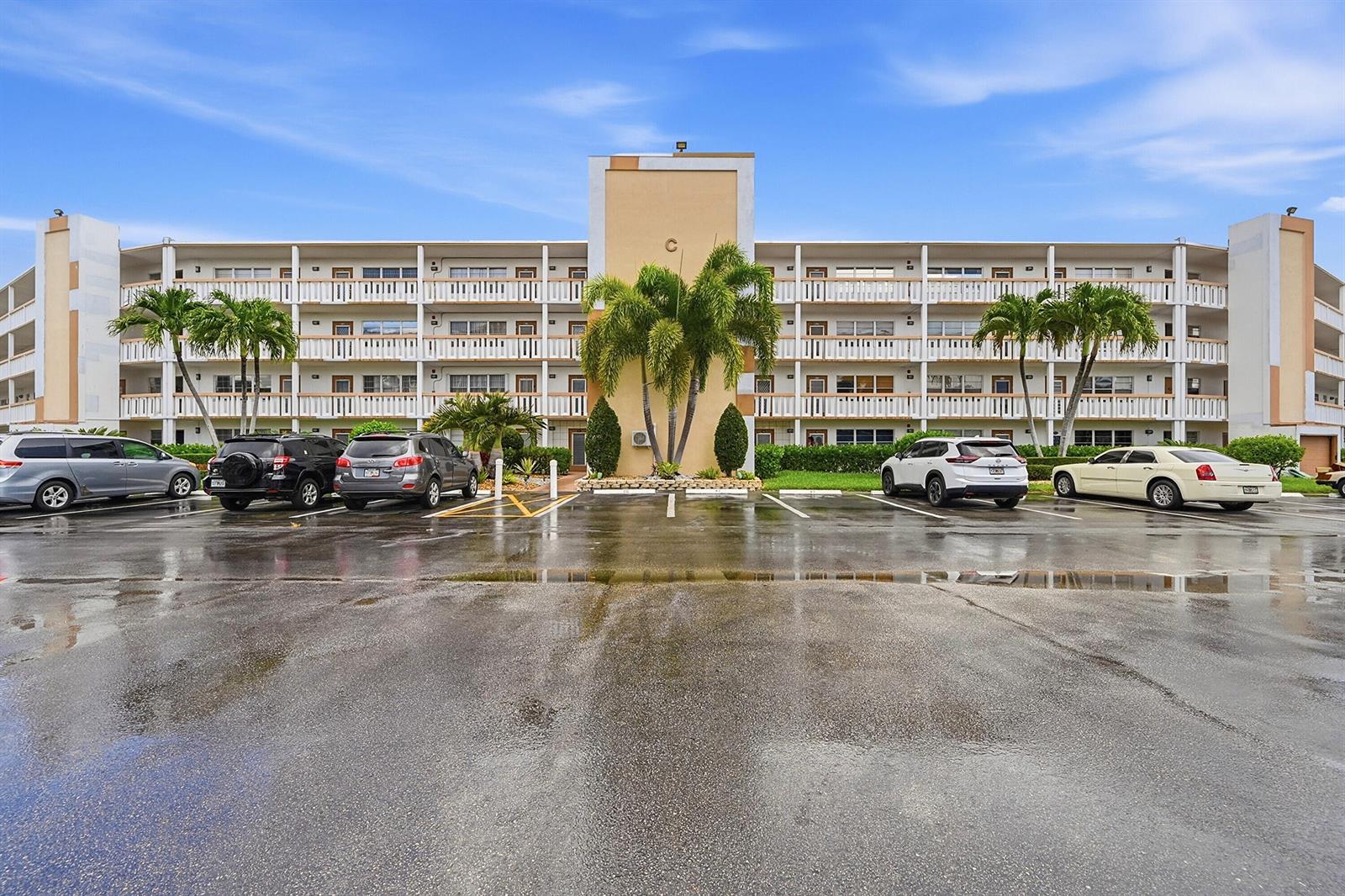 A multi-story apartment building with a parking lot in the foreground under a blue sky — 1043 Cornwall C, Boca Raton FL 33434, BOCA RATON, FL