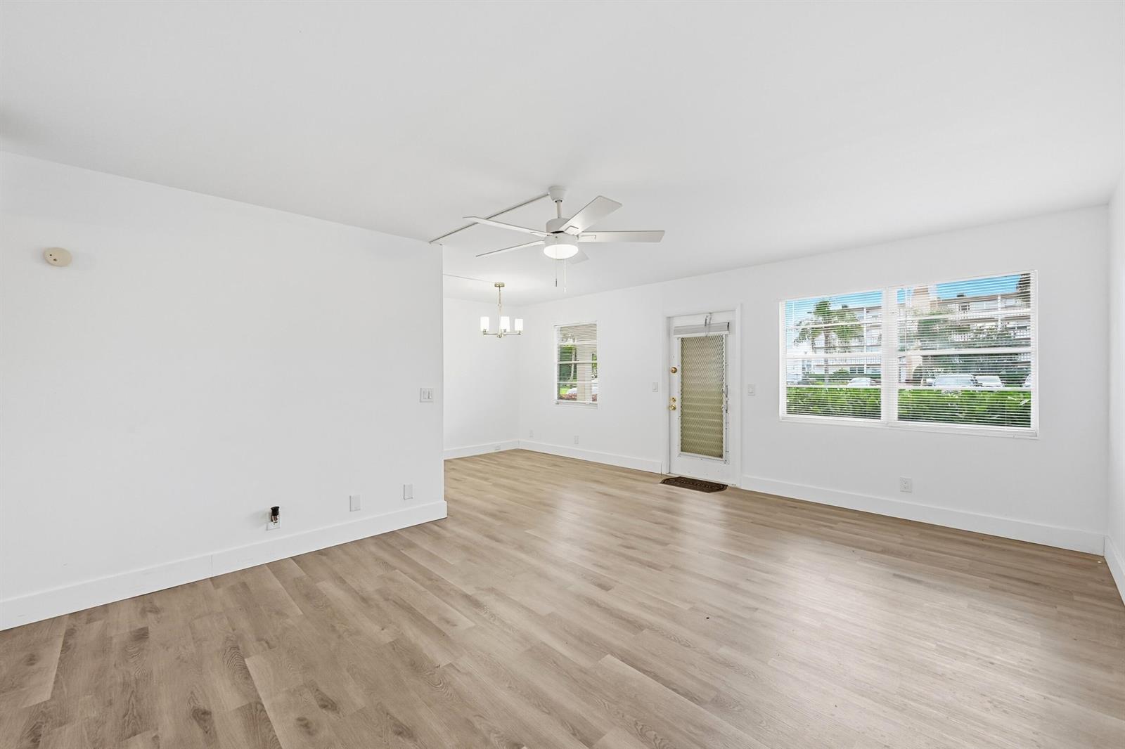 An empty living room features white walls, light wood-look flooring, a ceiling fan, and windows — 1043 Cornwall C, Boca Raton FL 33434, BOCA RATON, FL