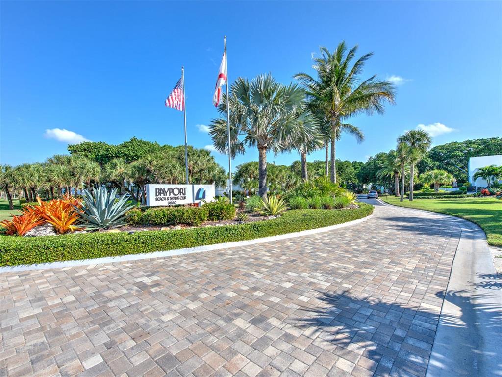 A paved driveway leads to the entrance sign of a residential community with palm trees — 517 BAYPORT WAY UNIT 517, LONGBOAT KEY, FL
