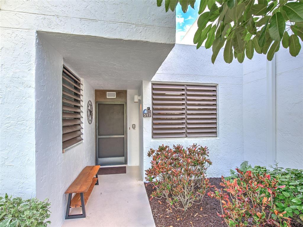 The exterior entrance features a white stucco wall, brown louvered shutters, and a wooden bench — 517 BAYPORT WAY UNIT 517, LONGBOAT KEY, FL