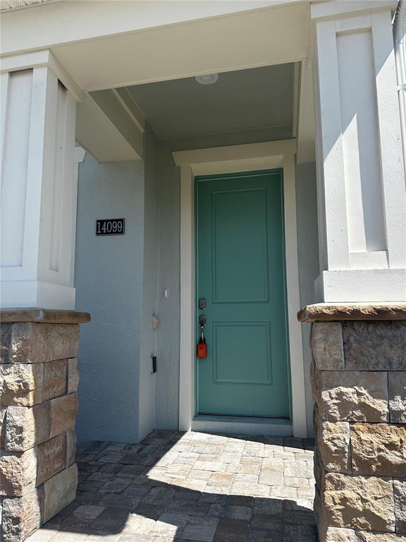 A teal front door is framed by white columns and stone bases on a paved porch — 14099 LOCHEND WAY, WINTER GARDEN, FL