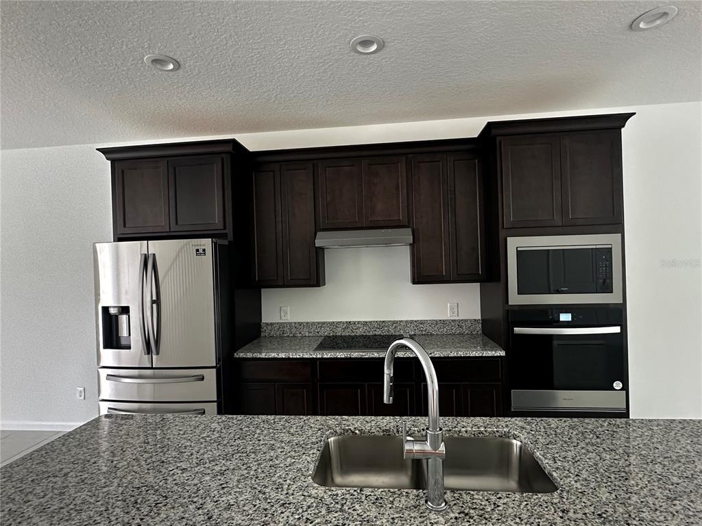 A kitchen features dark wood cabinets, granite countertops, stainless steel appliances, and a central island — 14099 LOCHEND WAY, WINTER GARDEN, FL