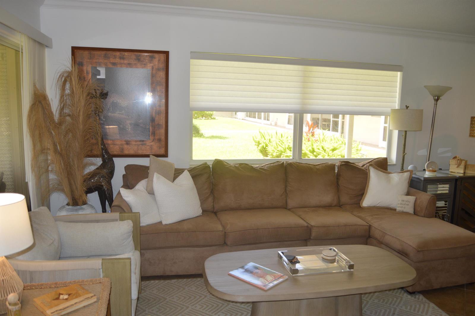 A living room features a brown sectional sofa, a coffee table, and a large window — 745 SE 19th Avenue # 114, Deerfield Beach FL 33441, DEERFIELD BEACH, FL