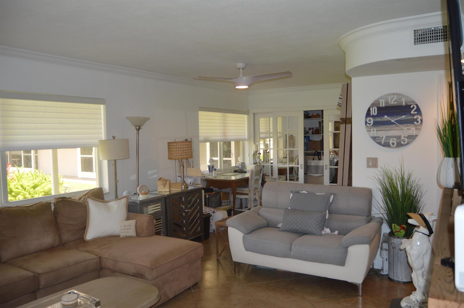 A living room features a brown sectional, a gray sofa, and a large wall clock — 745 SE 19th Avenue # 114, Deerfield Beach FL 33441, DEERFIELD BEACH, FL