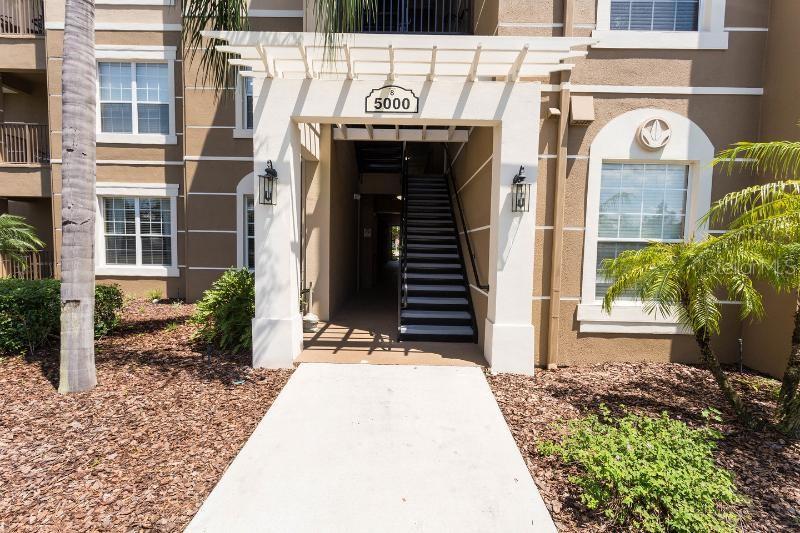 The exterior of a multi-story apartment building features a covered entrance with stairs — 5000 CAYVIEW AVENUE UNIT 309, ORLANDO, FL