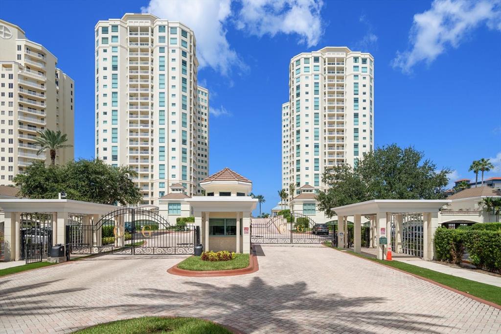 A gated entrance leads to two tall residential towers under a bright blue sky — 1170 GULF BOULEVARD UNIT 404, CLEARWATER BEACH, FL