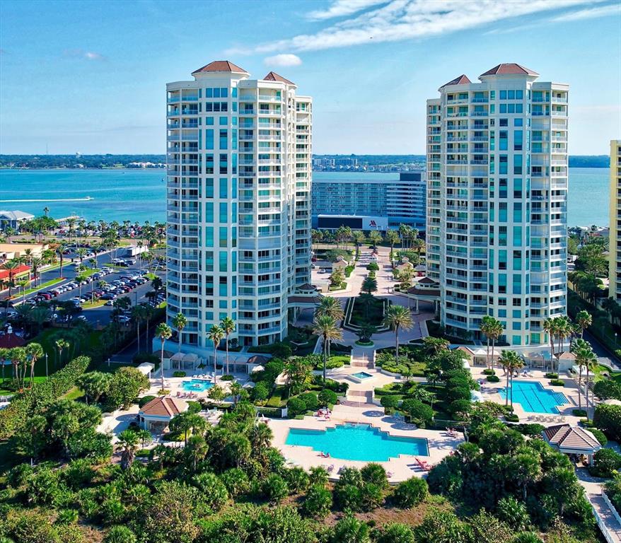 An aerial view shows two tall residential towers surrounded by swimming pools and lush landscaping — 1170 GULF BOULEVARD UNIT 404, CLEARWATER BEACH, FL