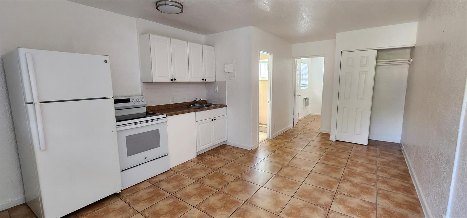 A kitchen with white cabinets, white appliances, and brown tile flooring in an open room — 620 NW 7th Avenue # 28, Pompano Beach FL 33060, POMPANO BEACH, FL