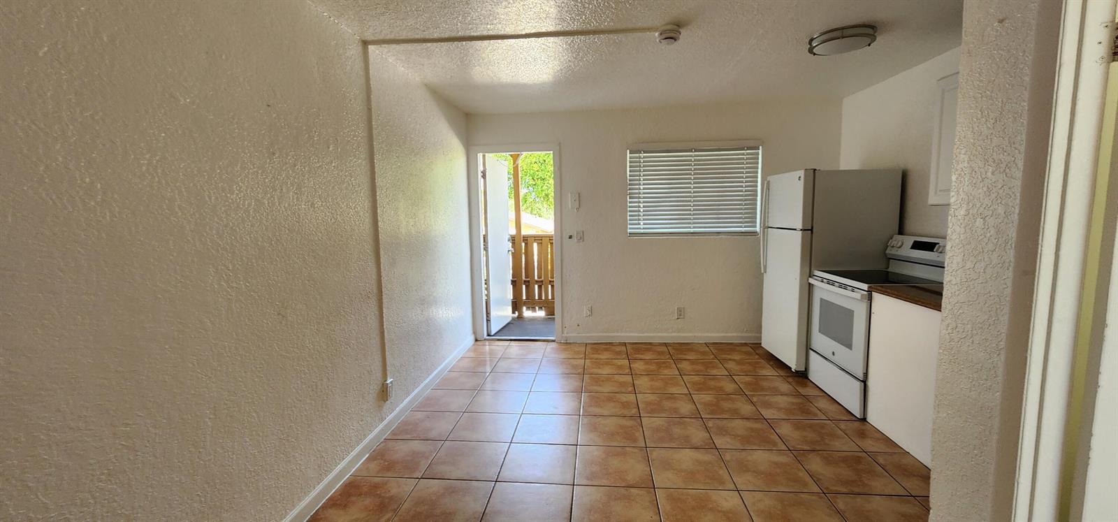 A kitchen with tile flooring, white appliances, and a door leading to an outdoor balcony — 620 NW 7th Avenue # 28, Pompano Beach FL 33060, POMPANO BEACH, FL