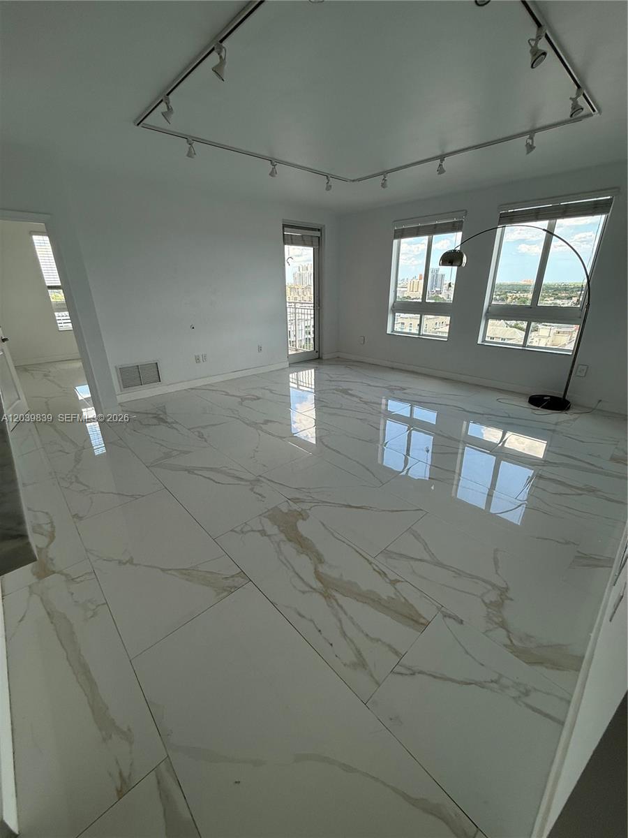 An empty room features white marble-look tile flooring, track lighting, and large windows with city views — 7350 SW 89th St # 1602S, Miami FL 33156, MIAMI, FL