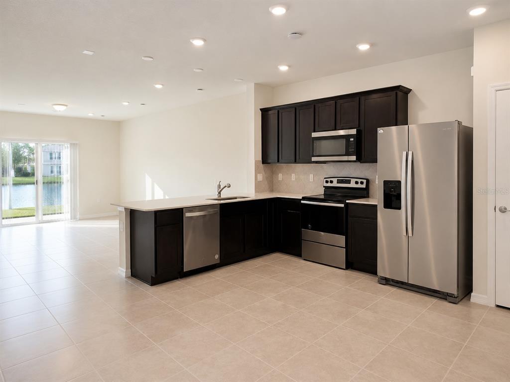 A kitchen with dark cabinets, stainless steel appliances, and tile flooring overlooks a lake view — 4576 SPARKLING SHELL AVENUE, KISSIMMEE, FL