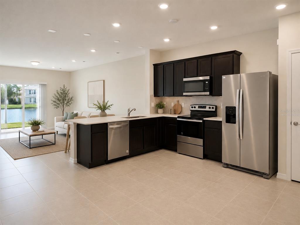 A kitchen with dark cabinets and stainless steel appliances overlooks a living area and lake — 4576 SPARKLING SHELL AVENUE, KISSIMMEE, FL