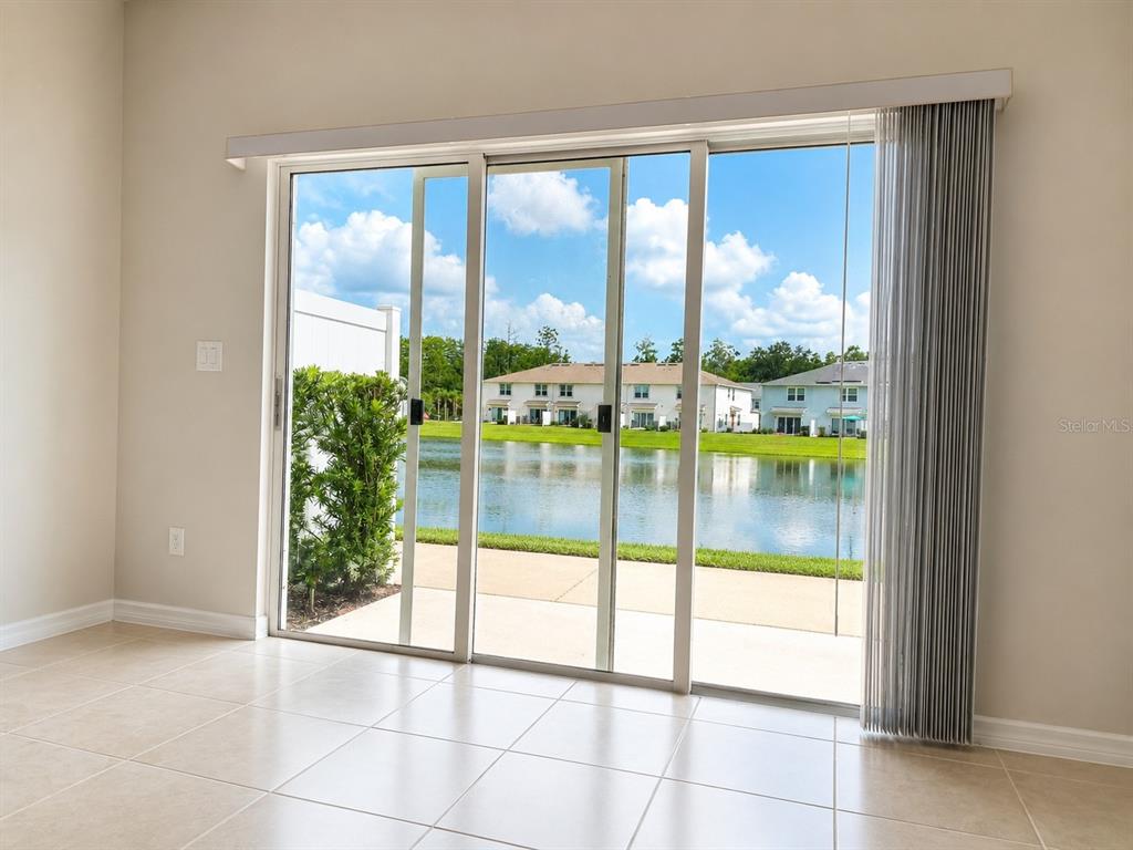 A room with light tile flooring features a large sliding glass door overlooking a pond — 4576 SPARKLING SHELL AVENUE, KISSIMMEE, FL