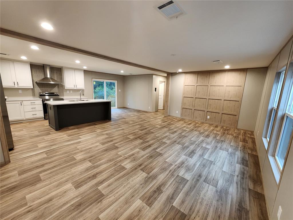 An open-concept kitchen and living area featuring wood-look flooring, white cabinetry, and a paneled wall — 7513 W DUNKLIN STREET, DUNNELLON, FL