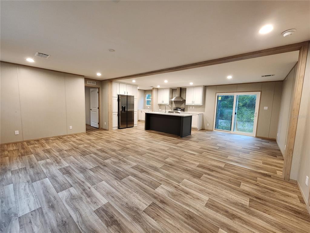 An open-concept kitchen and living area features wood-look flooring, white cabinetry, and a dark island — 7513 W DUNKLIN STREET, DUNNELLON, FL