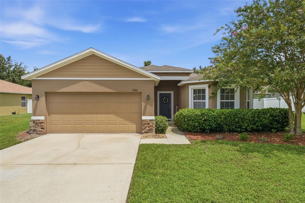 A single-story house with a tan stucco exterior, a two-car garage, and a front lawn — 940 FALLBROOKE AVENUE, DELTONA, FL