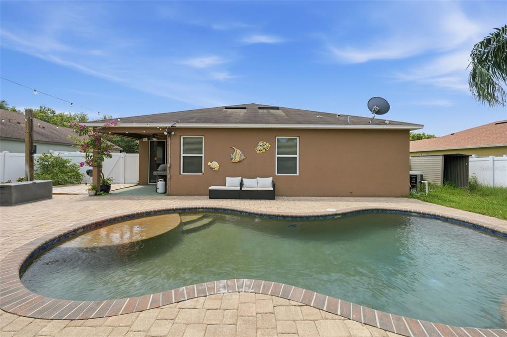 A backyard features a swimming pool with a tanning ledge and a tan house exterior — 940 FALLBROOKE AVENUE, DELTONA, FL