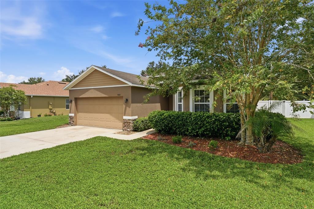 A tan single-story house with a two-car garage, a front lawn, and a large tree — 940 FALLBROOKE AVENUE, DELTONA, FL