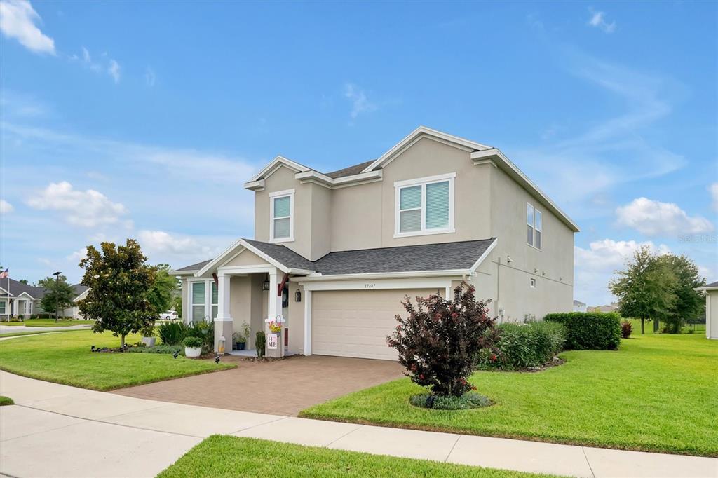 A two-story suburban house with a beige stucco exterior, a two-car garage, and a lawn — 17807 PASSIONFLOWER CIRCLE, CLERMONT, FL