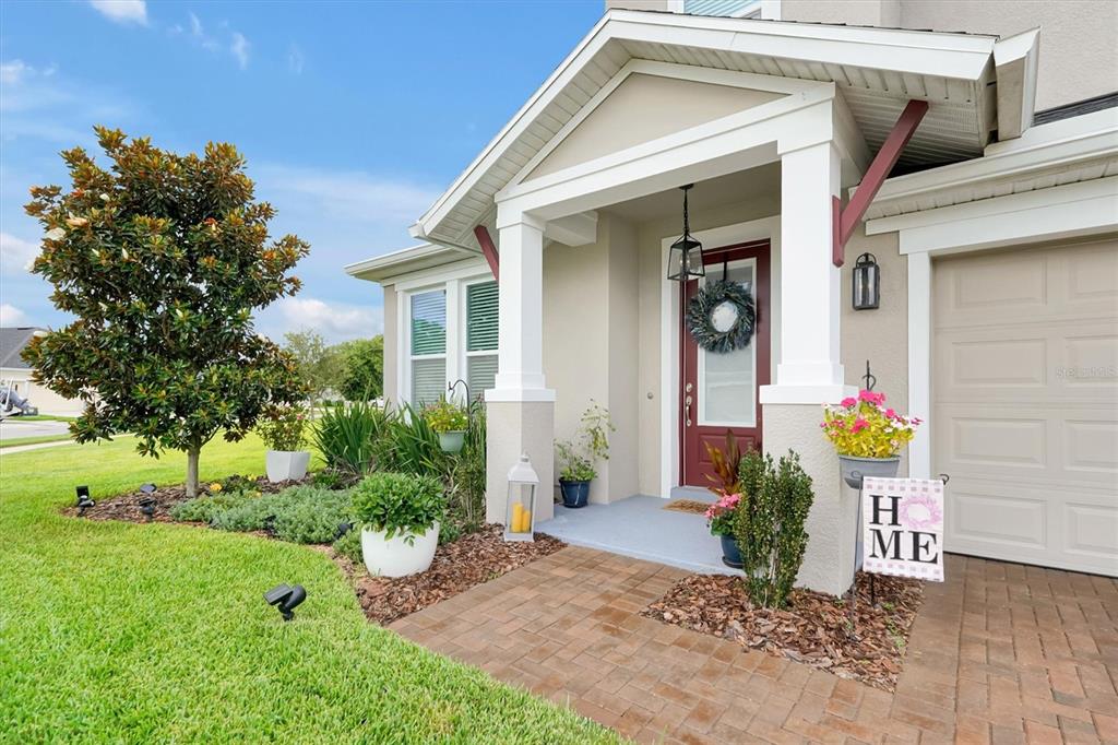 A beige house exterior features a covered entryway with a red door and brick walkway — 17807 PASSIONFLOWER CIRCLE, CLERMONT, FL