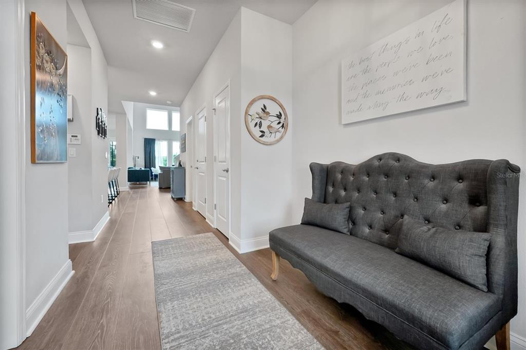 A hallway features wood-look flooring, a grey tufted settee, and wall art — 17807 PASSIONFLOWER CIRCLE, CLERMONT, FL