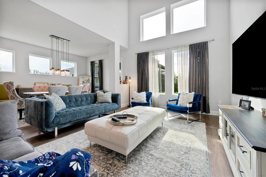 A living room features a blue velvet sofa, white ottoman, and high ceilings with windows — 17807 PASSIONFLOWER CIRCLE, CLERMONT, FL