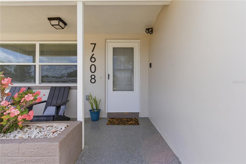 A covered front porch features a white door, house numbers, and a small potted plant — 7608 SUE ELLEN DRIVE, PORT RICHEY, FL