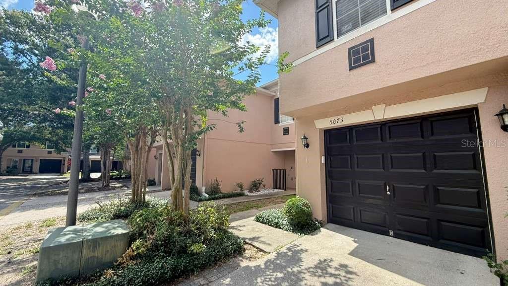 A two-story townhouse exterior features a dark garage door, light stucco walls, and landscaping — 5073 KINGSCREST LANE, OVIEDO, FL