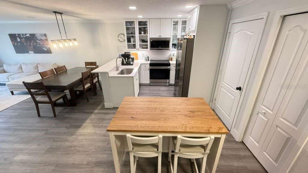 A kitchen with white cabinets, stainless steel appliances, and a wooden island with two chairs — 5073 KINGSCREST LANE, OVIEDO, FL