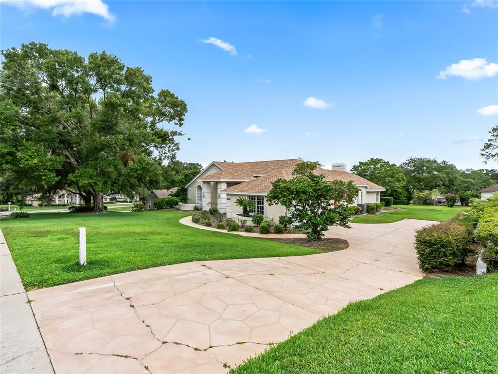 A single-story house with a tan roof and a cracked concrete driveway sits on grass — 5321 GREENS DRIVE, LADY LAKE, FL