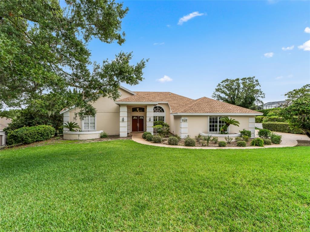 A single-story house with a tan exterior, a brown shingled roof, and a large lawn — 5321 GREENS DRIVE, LADY LAKE, FL