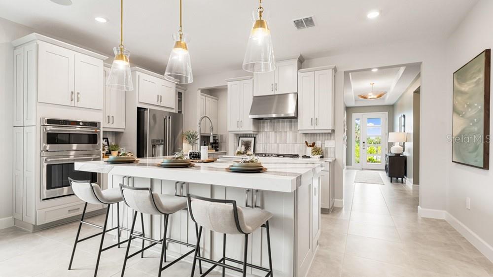 A modern kitchen features white cabinetry, a large center island with seating, and stainless appliances — 12751 DOCKYARD TRAIL, PALMETTO, FL