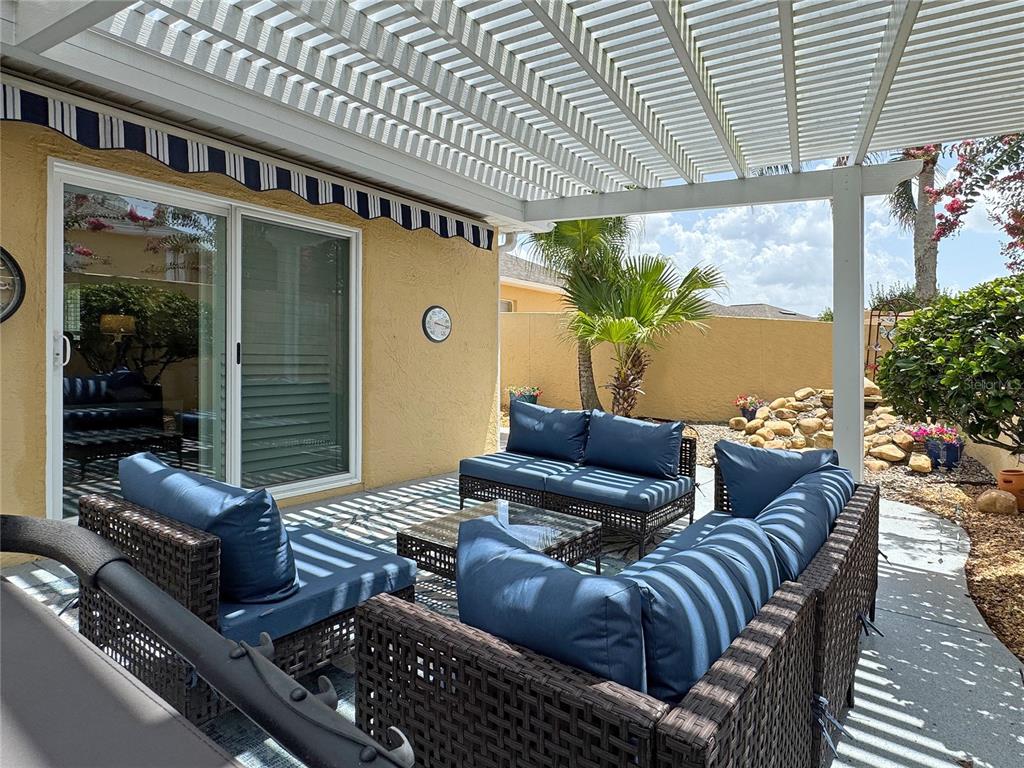 A patio features wicker furniture with blue cushions under a white pergola and awning — 896 RADCLIFE BEREA PLACE, THE VILLAGES, FL