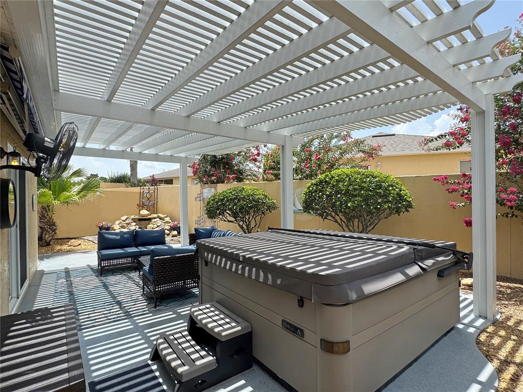 A patio features a hot tub, outdoor seating, and a white pergola under a blue sky — 896 RADCLIFE BEREA PLACE, THE VILLAGES, FL
