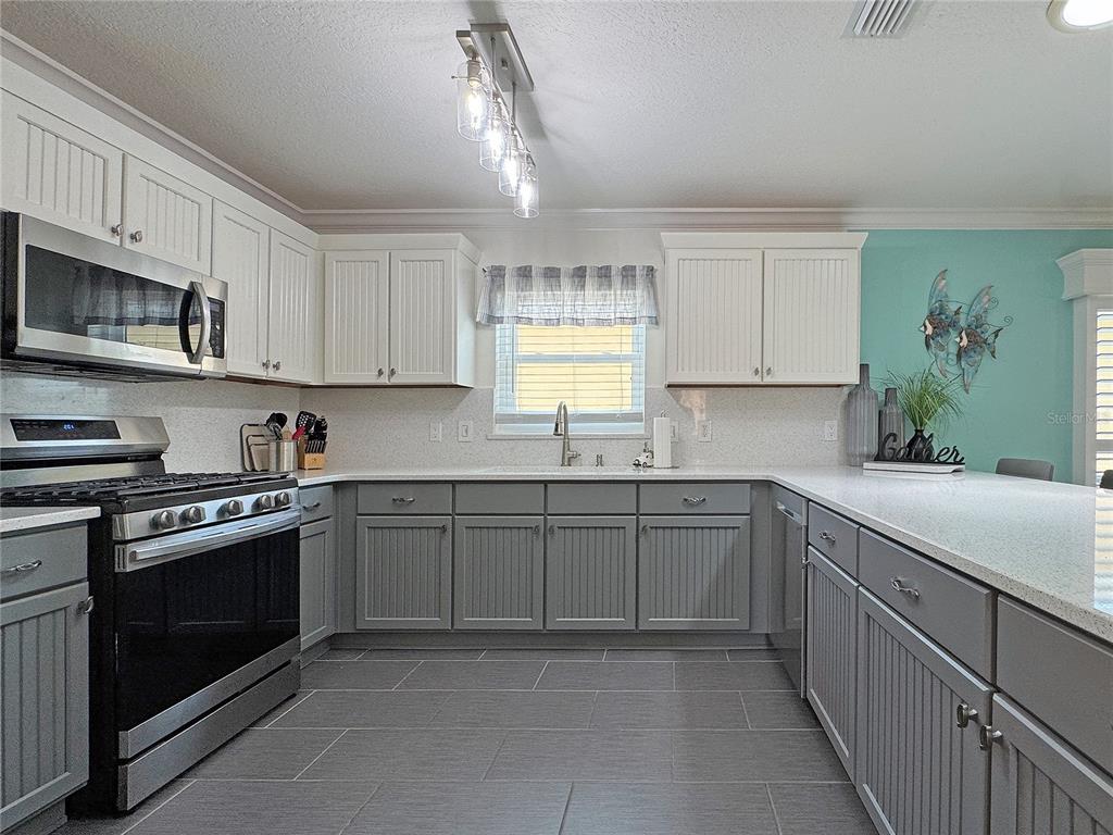 A kitchen features two-toned cabinetry, stainless steel appliances, and gray tile flooring — 896 RADCLIFE BEREA PLACE, THE VILLAGES, FL