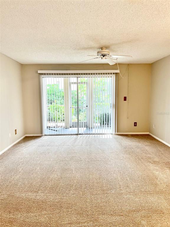 An empty living room features beige carpeting, a ceiling fan, and sliding glass patio doors — 506 ORANGE DRIVE UNIT 15, ALTAMONTE SPRINGS, FL