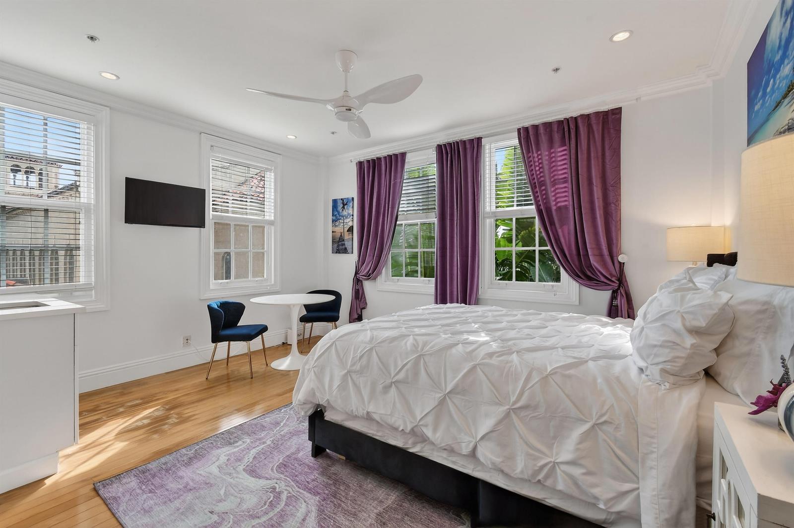 A bedroom features a white bed, purple curtains, a small dining table, and hardwood floors — 235 Sunrise Avenue # 3265, Palm Beach FL 33480, PALM BEACH, FL