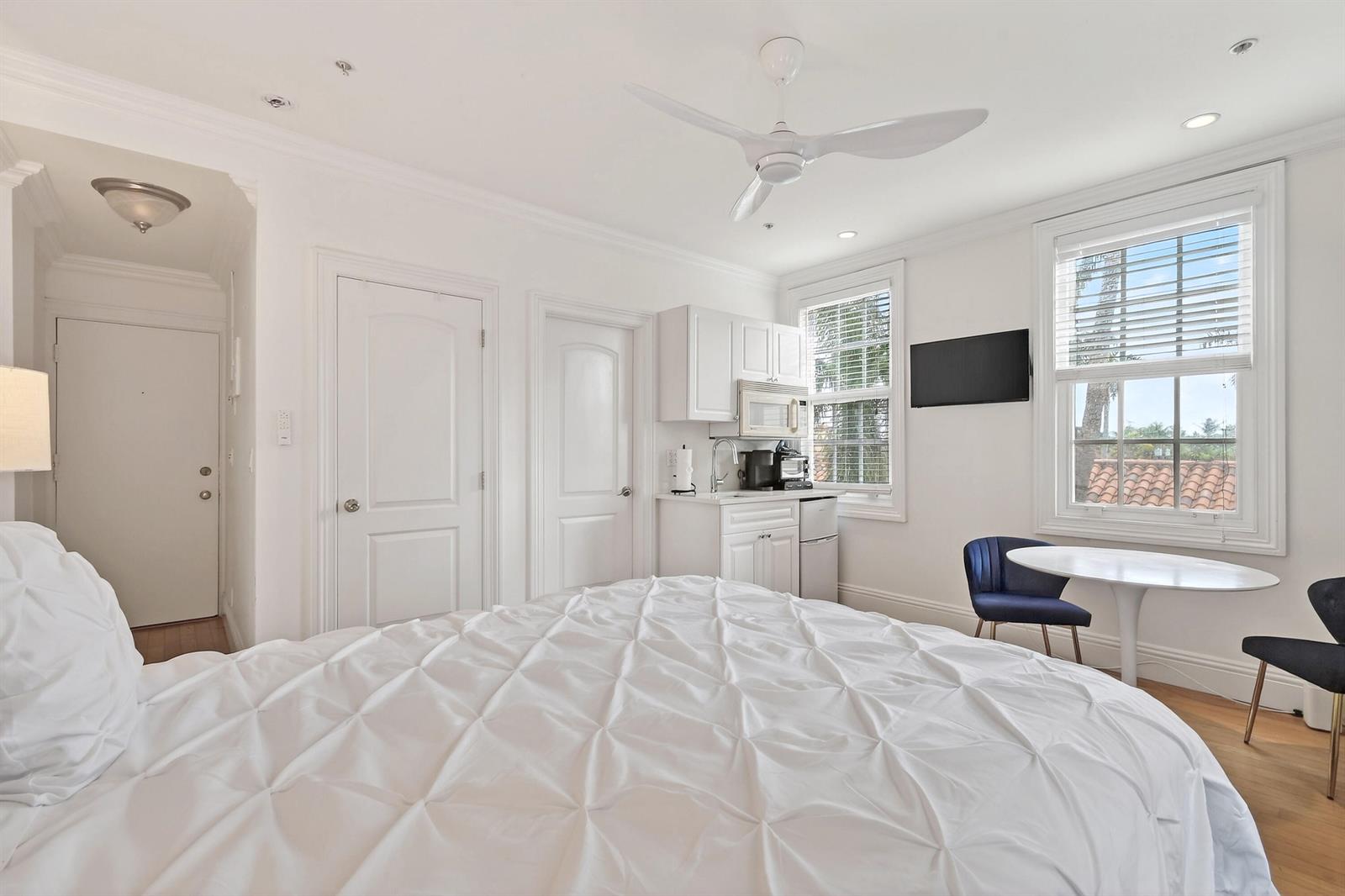 A bedroom features a white bed, a small kitchenette, a dining set, and two windows — 235 Sunrise Avenue # 3265, Palm Beach FL 33480, PALM BEACH, FL