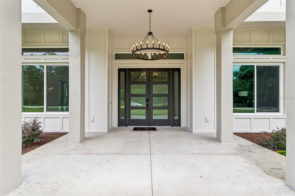 A covered front porch features a dark double door, a chandelier, and large windows — 12000 GOLDEN VALLEY DRIVE, NEW PORT RICHEY, FL