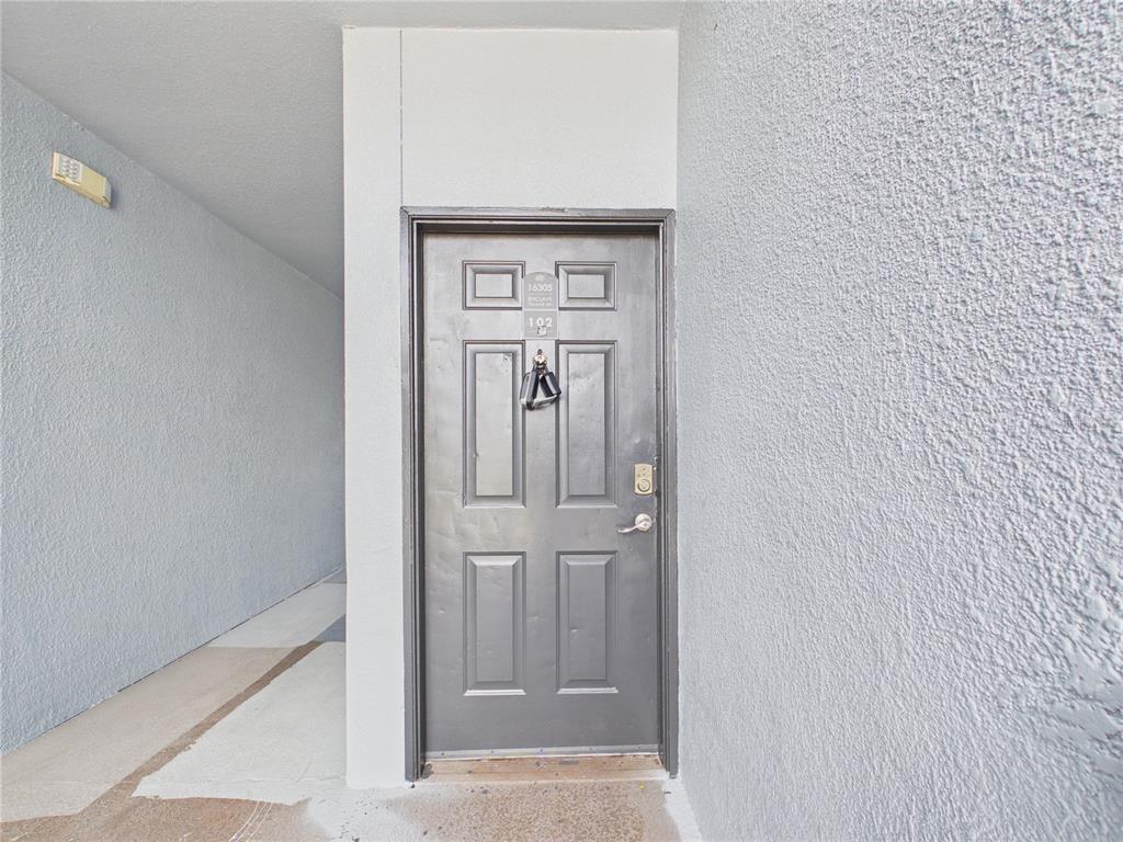 A dark gray front door with a lockbox is set into a textured light-colored wall — 16305 ENCLAVE VILLAGE DRIVE UNIT 102, TAMPA, FL