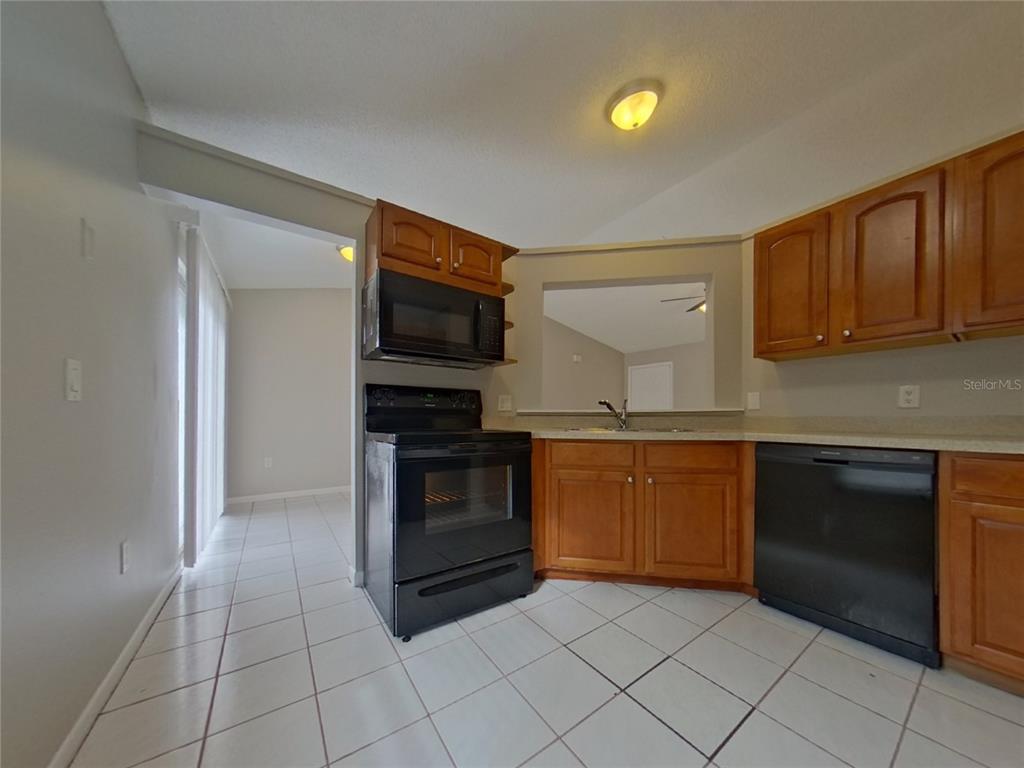 A kitchen with wood cabinets, black appliances, and white tile flooring — 1627 PENDLETON STREET, DELTONA, FL