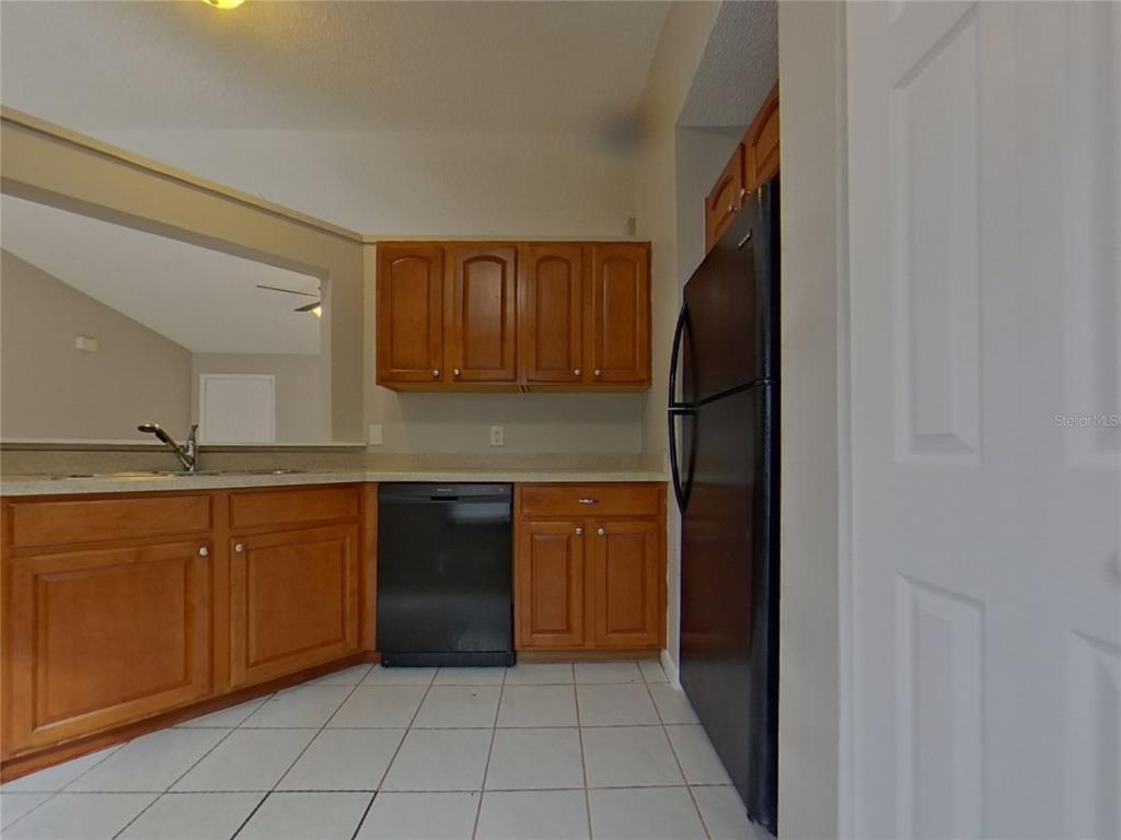 A kitchen features wood cabinets, black appliances, a tile floor, and a pass-through window — 1627 PENDLETON STREET, DELTONA, FL
