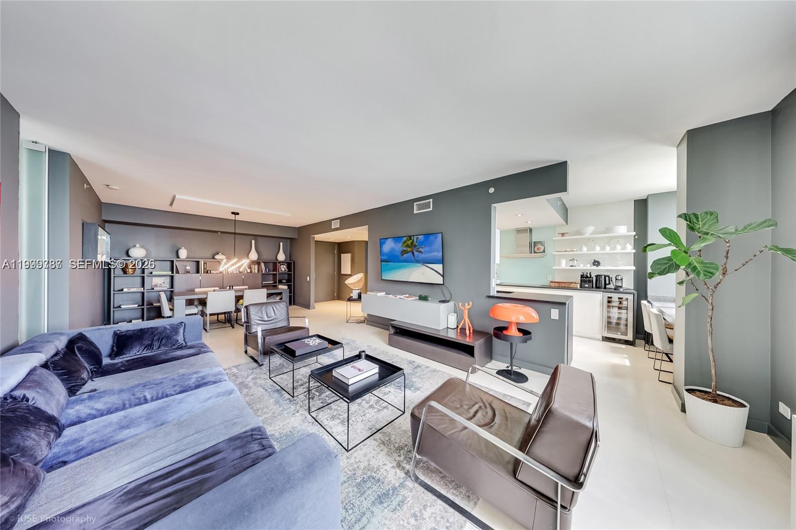 A modern living room features a blue sofa, leather armchairs, and an open kitchen area — 701 Brickell Key Blvd # 503, Miami FL 33131, MIAMI, FL